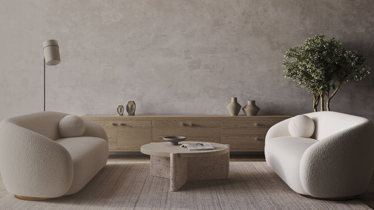 Neutral living room with boucle armchairs, a wood sideboard, and a round travertine coffee table