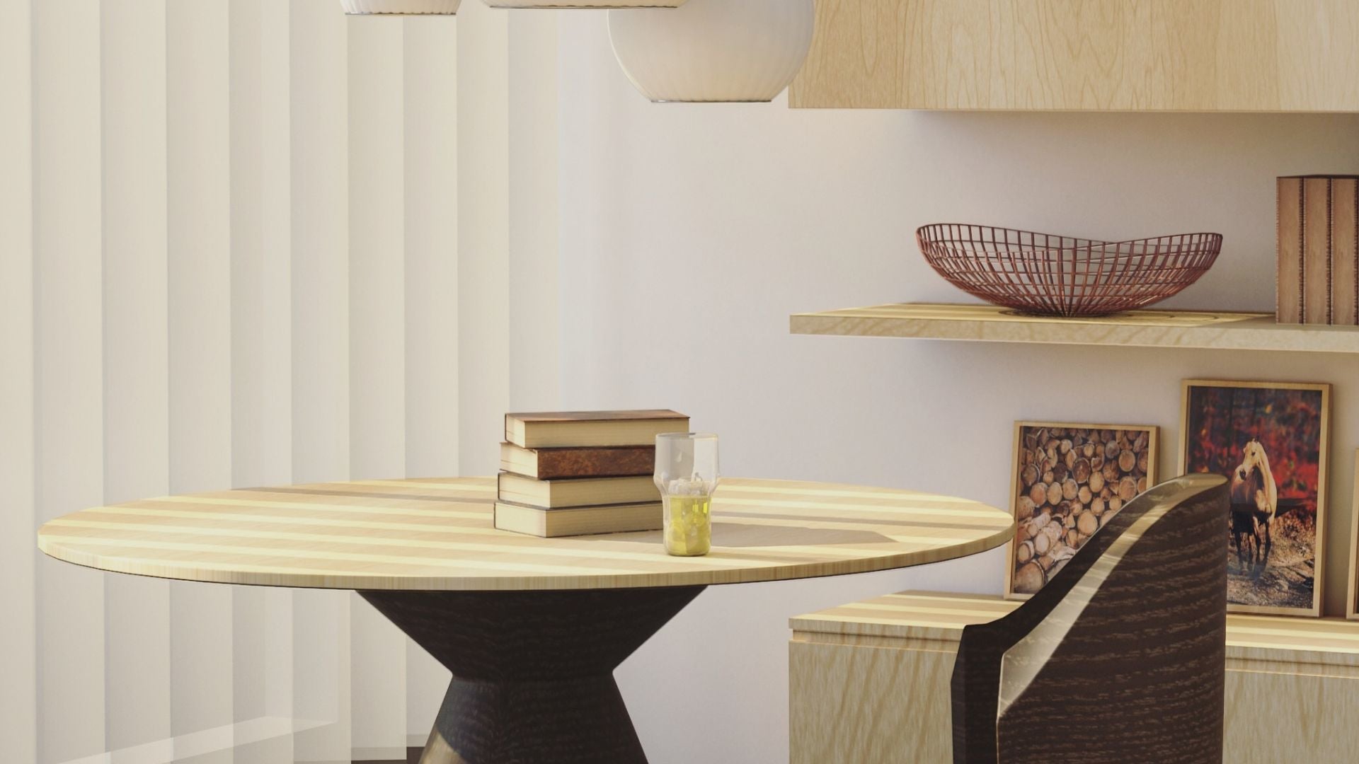 A modern round dining table with a light wood top and dark sculptural pedestal base, styled in a minimalist dining room setting with a chair, books, and a glass of lemonade.